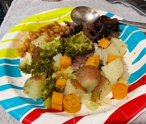 Paper plate with meat, baked beans and vegetables cooked in foil