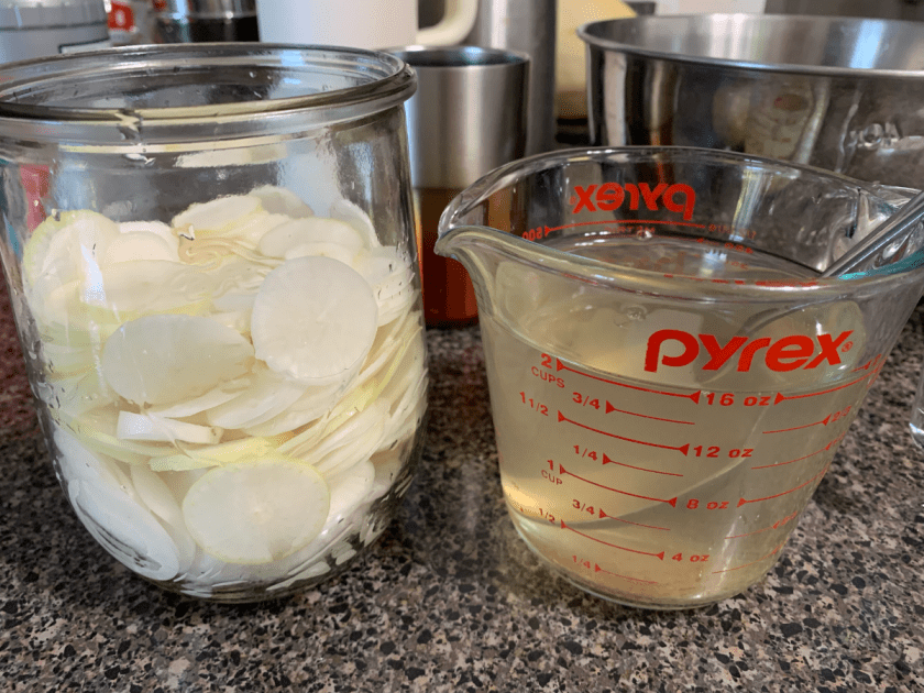 Daikon radish sliced into a Weck jar, with saltwater brine ready to pour in.
